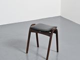 a small wooden chair with a black seat in a white room