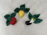 three small figurines of fruits and vegetables on a white surface