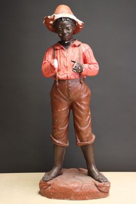 statue of a boy in a hat and brown pants holding a gun