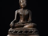 une statue en bronze représentant un Bouddha assis sur un fond noir