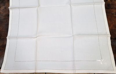 une serviette en lin blanche bordée d'une frange blanche, posée sur une table en bois