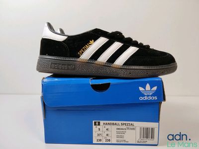une paire de baskets Adidas noires et blanches posée sur une boîte bleue