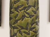 a large green vase sitting on a table with pictures on the wall behind it