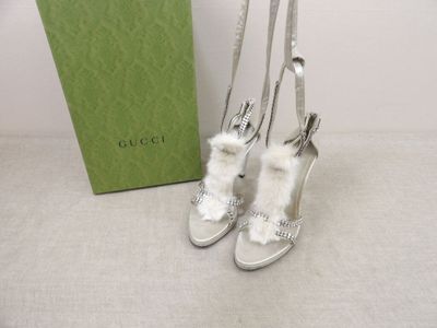 des chaussures Gucci ornées de fourrure blanche et dotées de talons argentés, posées à côté d'une boîte verte