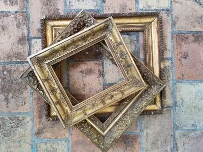 quatre cadres dorés accrochés à un mur en briques, à côté d'un sol en briques