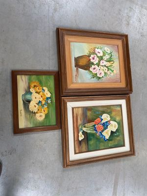 trois tableaux accrochés au mur au-dessus d'un vase de fleurs