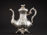 une cafetière ancienne en argent posée sur un support, sur fond noir