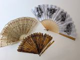 Trois vieux ventilateurs sont posés sur une surface blanche ; l'un est ouvert et l'autre fermé.