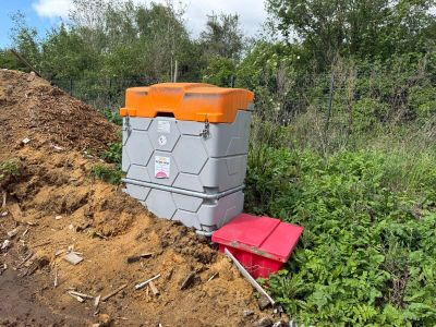 une glacière orange et grise posée sur un tas de terre, à côté d'un autre tas de terre