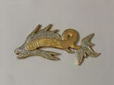 a gold and silver fish brooch on a white surface