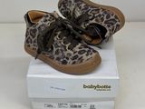 des chaussures de bébé à imprimé léopard posées sur une boîte, sur une surface blanche