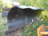 a black plow sitting in the grass next to a yellow bucket