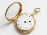 une montre de poche en or posée sur une surface blanche