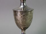 an antique silver cup with a lid on a metal stand