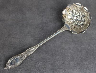 une cuillère ancienne en argent, ornée d'un motif floral sur un fond gris