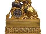 a gold clock with a woman sitting on top of it