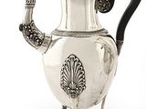 a silver teapot with a black handle on a stand