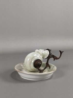 une assiette blanche sur laquelle est représenté un escargot, posée sur un fond gris