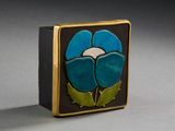 une fleur bleue et verte sur une boîte noire et dorée posée sur une surface grise