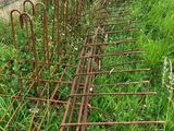 several rusty iron fence posts in the grass next to a building