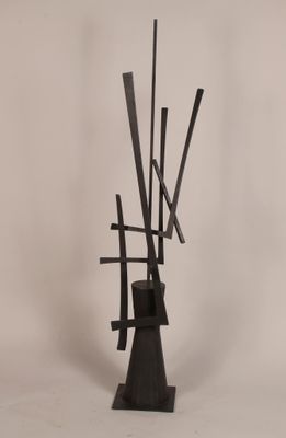 une sculpture noire composée de bâtons sortant d'un vase posé sur une surface blanche