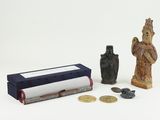 une petite statue à côté d'un petit livre et de quelques pièces de monnaie