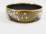 a close up of a black and gold bangle with a fish design