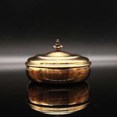 an antique gold plated bowl with a lid on a black surface