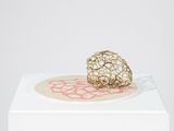 sculpture représentant une boule dorée posée sur un socle blanc orné d'un motif rouge