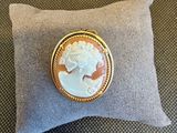 une broche en camée dorée et blanche posée sur un coussin