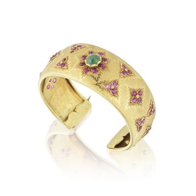 un gros plan d'une bague en or sertie de pierres roses et vertes