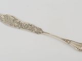 une cuillère en argent ornée d'un motif décoratif, posée sur une surface blanche