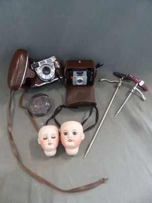 un appareil photo, un casque audio, une paire de lunettes, une paire de ciseaux et deux têtes de poupées
