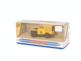 un petit camion jaune dans une boîte, posé sur une surface blanche