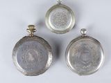 three antique silver pocket watches are displayed on a white surface