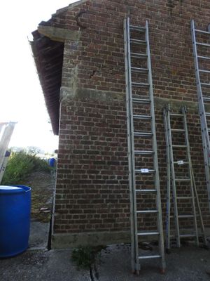 several ladders are leaning against a brick wall near a blue barrel