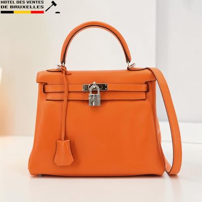 un petit sac Hermès orange posé sur une table, à côté d'une plante en pot