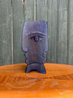 une statue bleue posée sur une table en bois, avec une clôture verte en arrière-plan