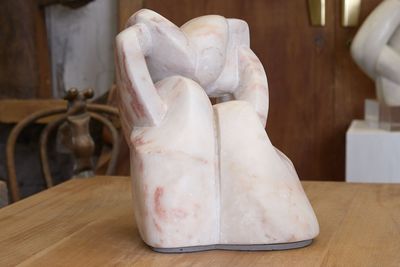 une sculpture en marbre blanc posée sur une table, avec une horloge en arrière-plan