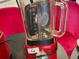 a red blender sitting on a table in front of a red chair