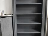 a black bookcase with shelves in the corner next to a trash can