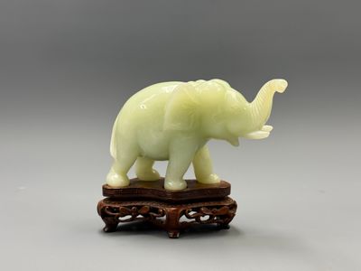 une statue d'éléphant posée sur un socle en bois, avec un fond gris en arrière-plan