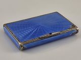 un étui à cigarettes ancien en argent et verre bleu posé sur une surface blanche
