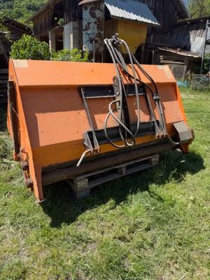 une charrue orange posée au milieu d'un champ vert, à côté d'une grange