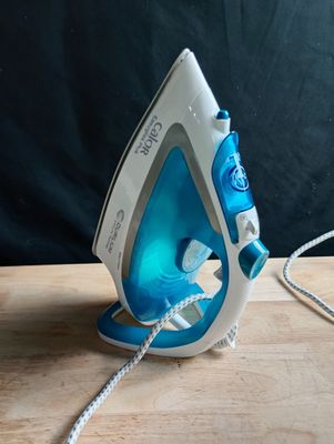 un fer à repasser à vapeur bleu et blanc posé sur une table en bois