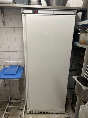 un petit réfrigérateur blanc dans une cuisine, avec un plateau bleu posé par terre