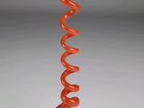 une sculpture en verre orange représentant un motif en spirale, posée sur un socle en marbre