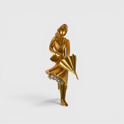 statue en or représentant une femme tenant un parapluie, posée sur une surface blanche