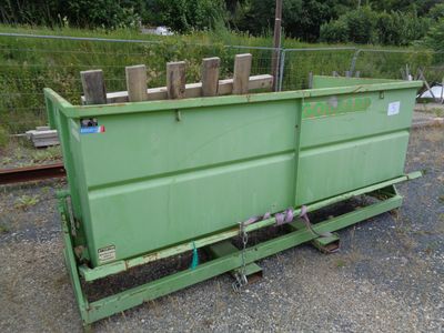 a green dumpster sitting on the side of a train track