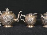 three silverplated teapots and two cups on a black background